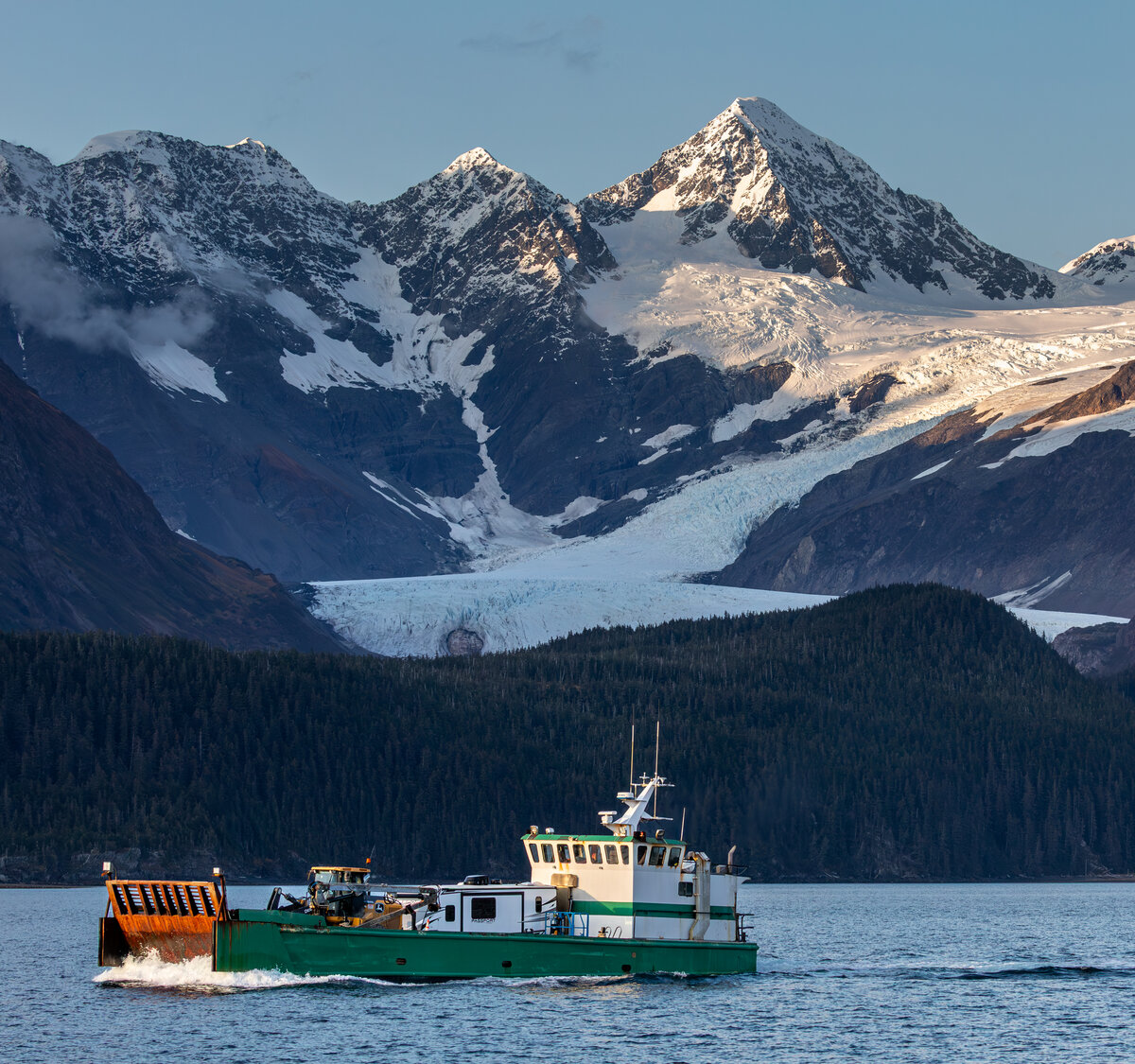 Commercial vessel transiting an Alaskan waterway beneath glaciated peaks
